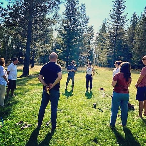 A group gathered in a circle on a tree-lined lawn